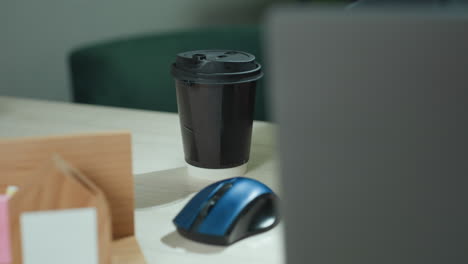 close up of real estate mogul setting disposable tea cup on modern desk beside laptop and mouse, preparing workstation for productive morning with wooden organizer