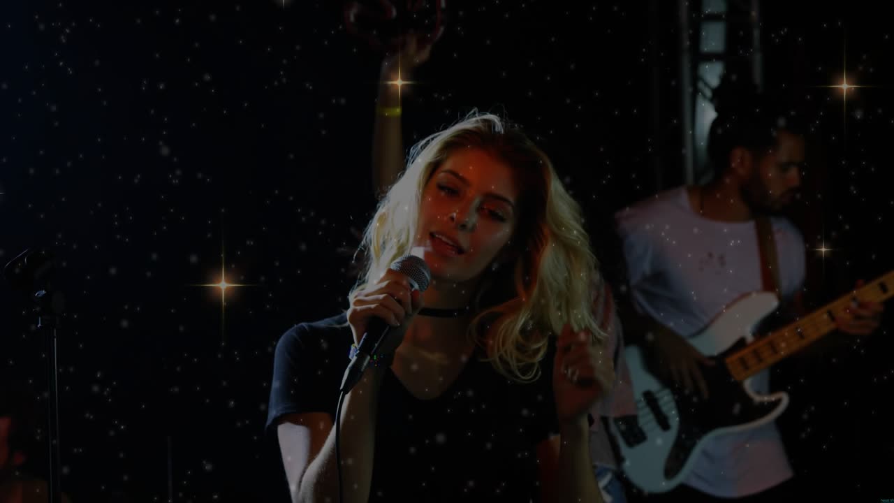 Lead vocalist performing on dim stage, band playing and music building sparkles accenting hair whip