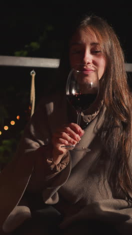 wife cheers wineglass with husband on terrace. young lady shares romantic candlelit dinner with partner in open-air restaurant among garlanded trees