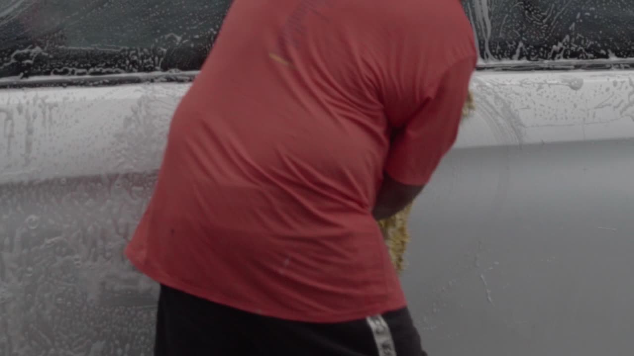 Person washing a car with a cloth outside during the day