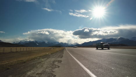 vehicles driving down highway with beautiful mountains and clouds in the background as the sun shines overhead