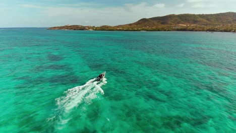 epic aerial of a speed boat making waves in the caribbean island of carriacou, grenada