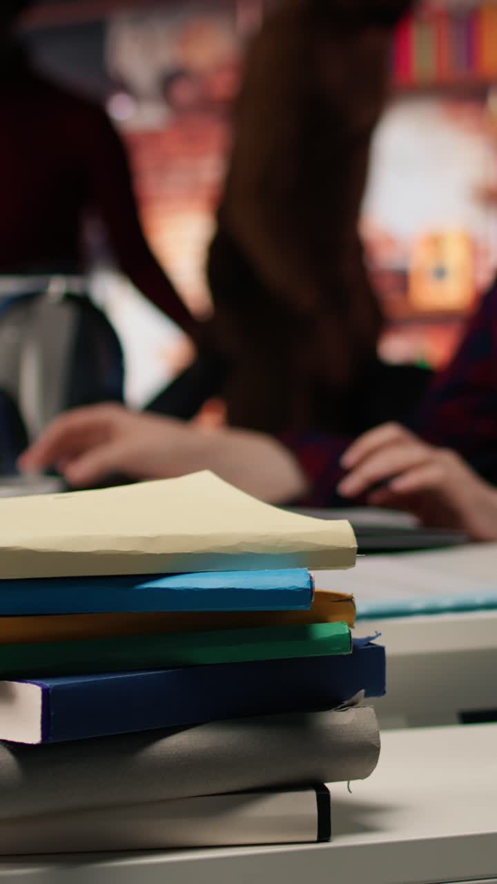 Vertical video Stack of books on startup office desk in front of woman working, closeup