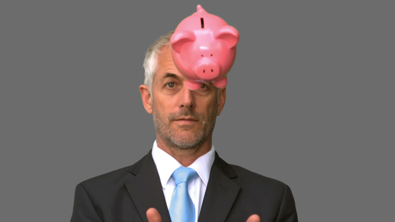 Geschäftsmann wirft ein Sparschwein vor grauem Hintergrund