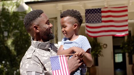 feliz soldado afroamericano abrazando a su hijo con bandera estadounidense, en cámara lenta