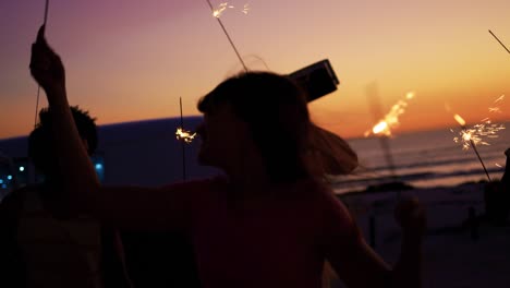 jóvenes amigos adultos divirtiéndose en la playa por la noche con chispas 4k