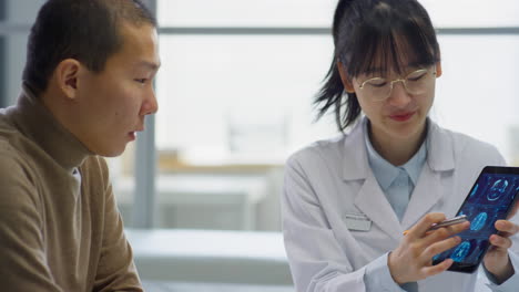 asian female doctor explaining x-ray on tablet to man