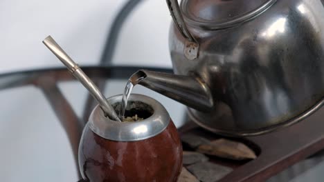 close up shot of person pouring down boiling water from kettle into pumpkin mate with straw preparing the local beverage of argentina and uruguay