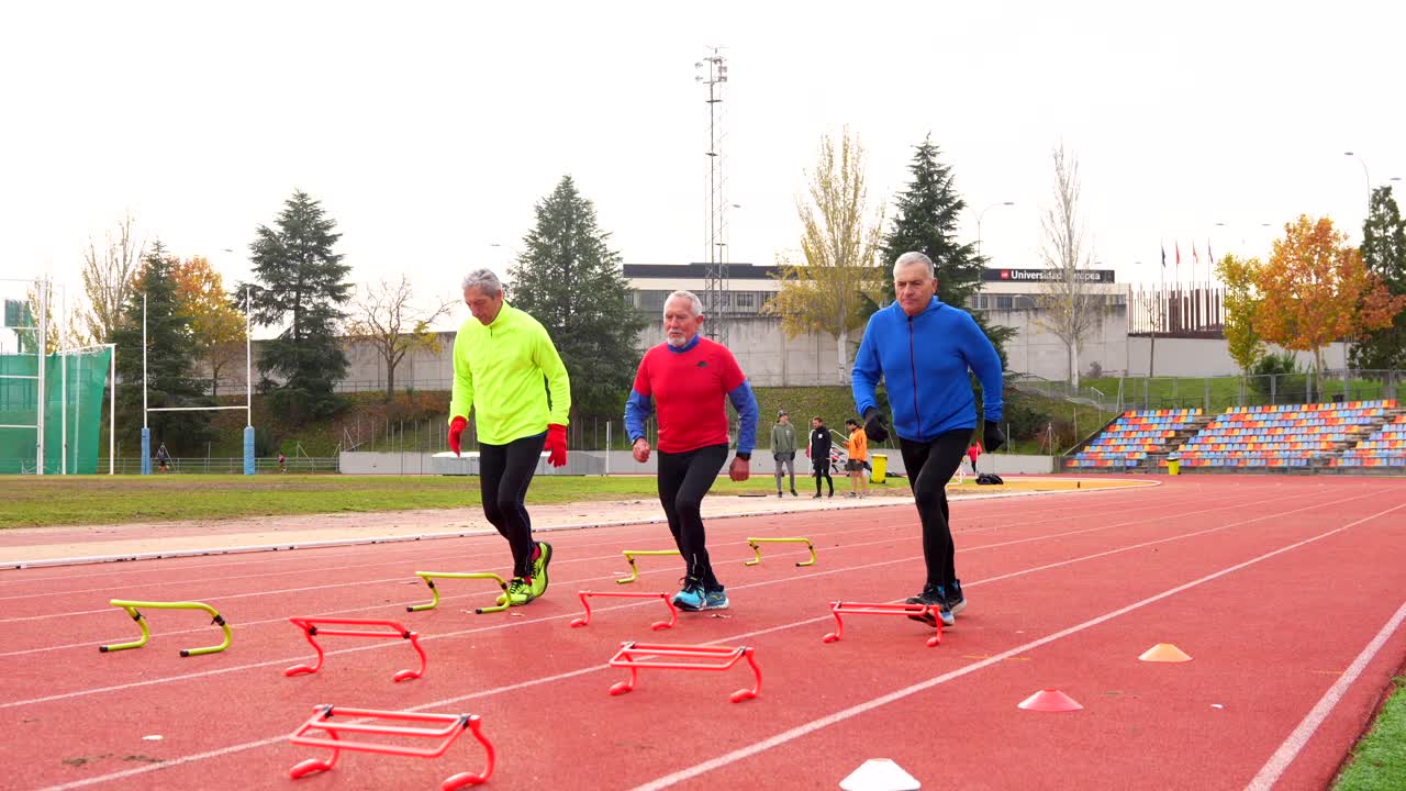 Older men running hurdles on a track