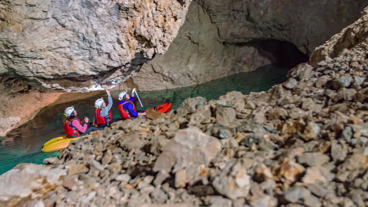 Three Caucasian women on kayak paddle in clear pristine water inside underground mining cave, slow motion pan
