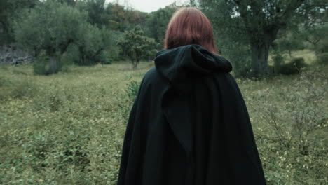 from back woman with red hair walks in a meadow among olive trees