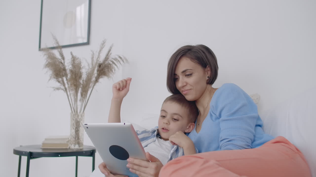 madre e hijo usando tableta digital en el dormitorio en casa. vista frontal de madre y hijo caucásicos felices usando tableta virtual en el dormitorio en casa