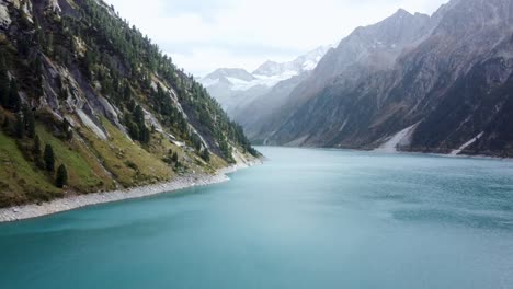 aerial view of turquoise lake amidst rugged mountains with distant snow peaks