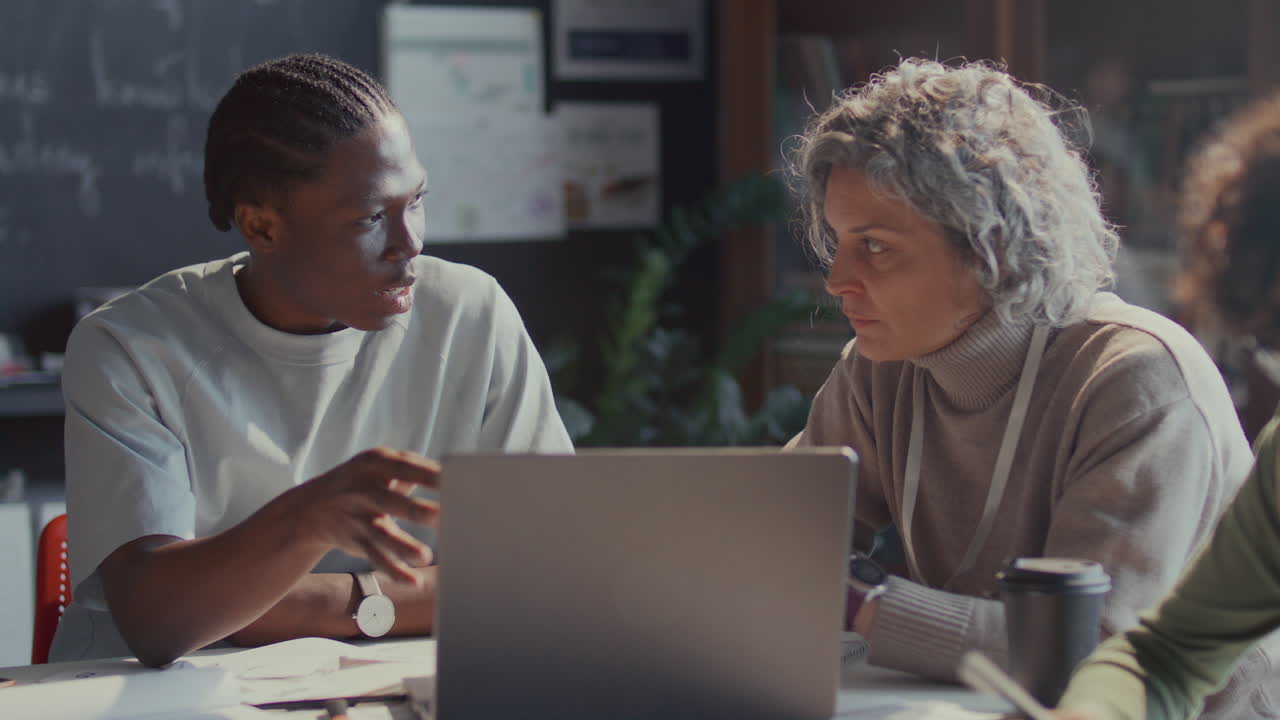 Black Student Discussing Assignment on Laptop with English Teacher