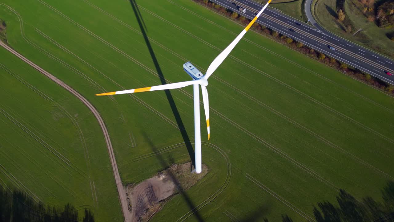 Wind turbine standing in green field next to highway autobahn in autumn Germany, generating renewable energy. Stunning aerial view flight overflight flyover drone