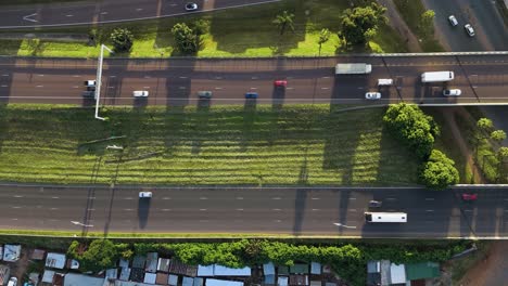 drone clip of a busy highway scene as cars and trucks pass a poor community on the side of the road