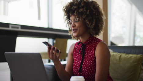 Mixed-race-woman-going-through-paperwork-talking-on-smartphone-using-laptop-in-the-office