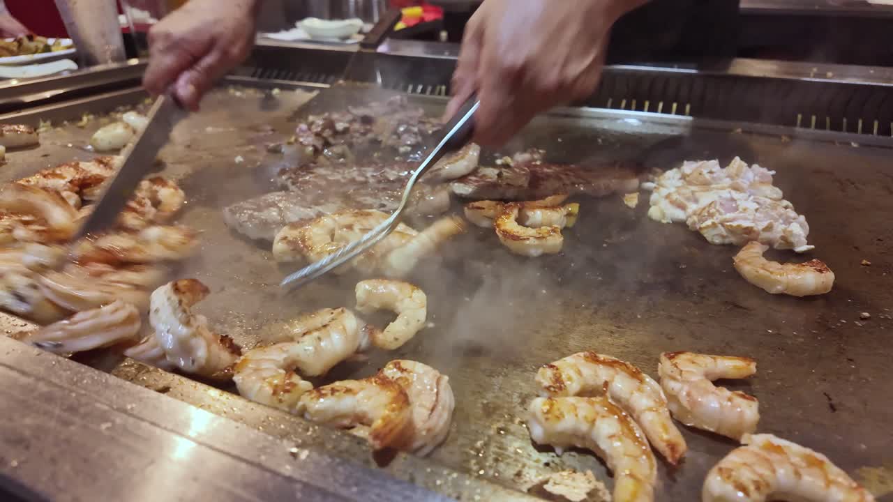 Chef cooks shrimp, scallops, steak, and chicken on hot teppanyaki grill, asian food and restaurant. Close-up