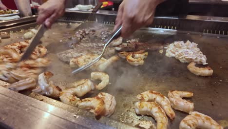 chef cooks shrimp, scallops, steak, and chicken on hot teppanyaki grill, asian food and restaurant. close-up