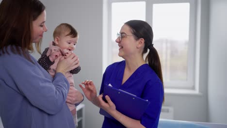 a happy brunette girl in a blue uniform communicates with a doctor along with her little child. childrens pediatrician and doctor for children communication. confident brunette girl with her little daughter at the girl childrens doctor in a modern clinic