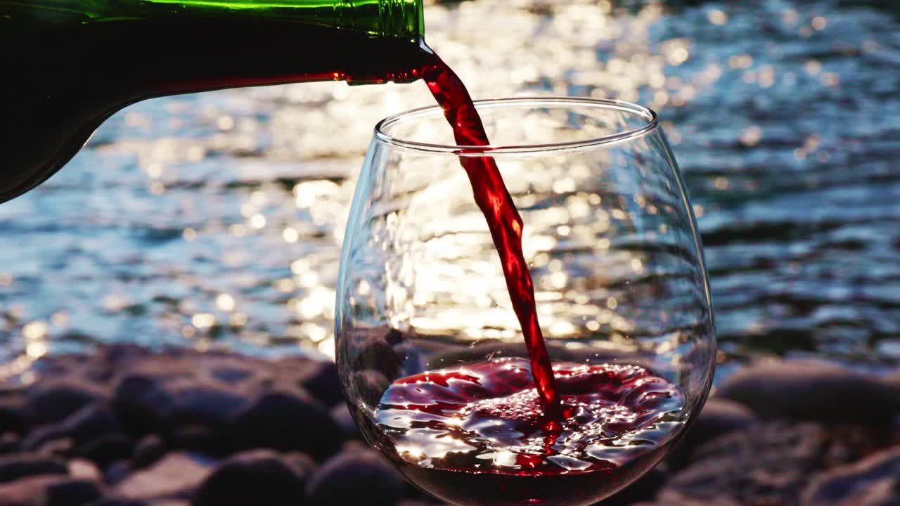 Versamento di Vino Rosso in Riva a un Fiume al Tramonto