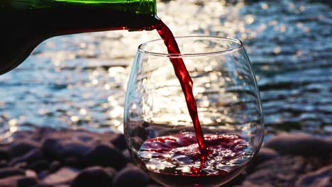 pouring red wine by a river at sunset