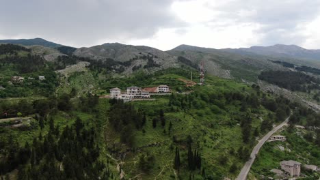 drone view in albania flying in gjirokaster over a medieval town showing green mountain with a hotel and brick brown roof houses