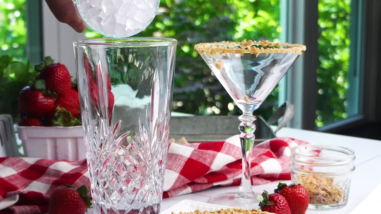 Strawberry Shortcake Martini cocktail with whipped cream, graham cracker crumbs and a fresh red strawberry. Making a cocktail for happy hour. Filling the crystal cocktail shaker with ice cubes.