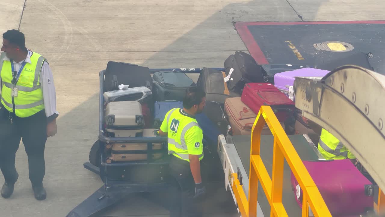 Ground crew members efficiently manage passenger luggage on the airport tarmac. The image shows baggage handlers performing their duties in a busy airport environment.