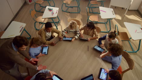 Male-teacher-helping-students-with-tablet-computers-at-lesson.