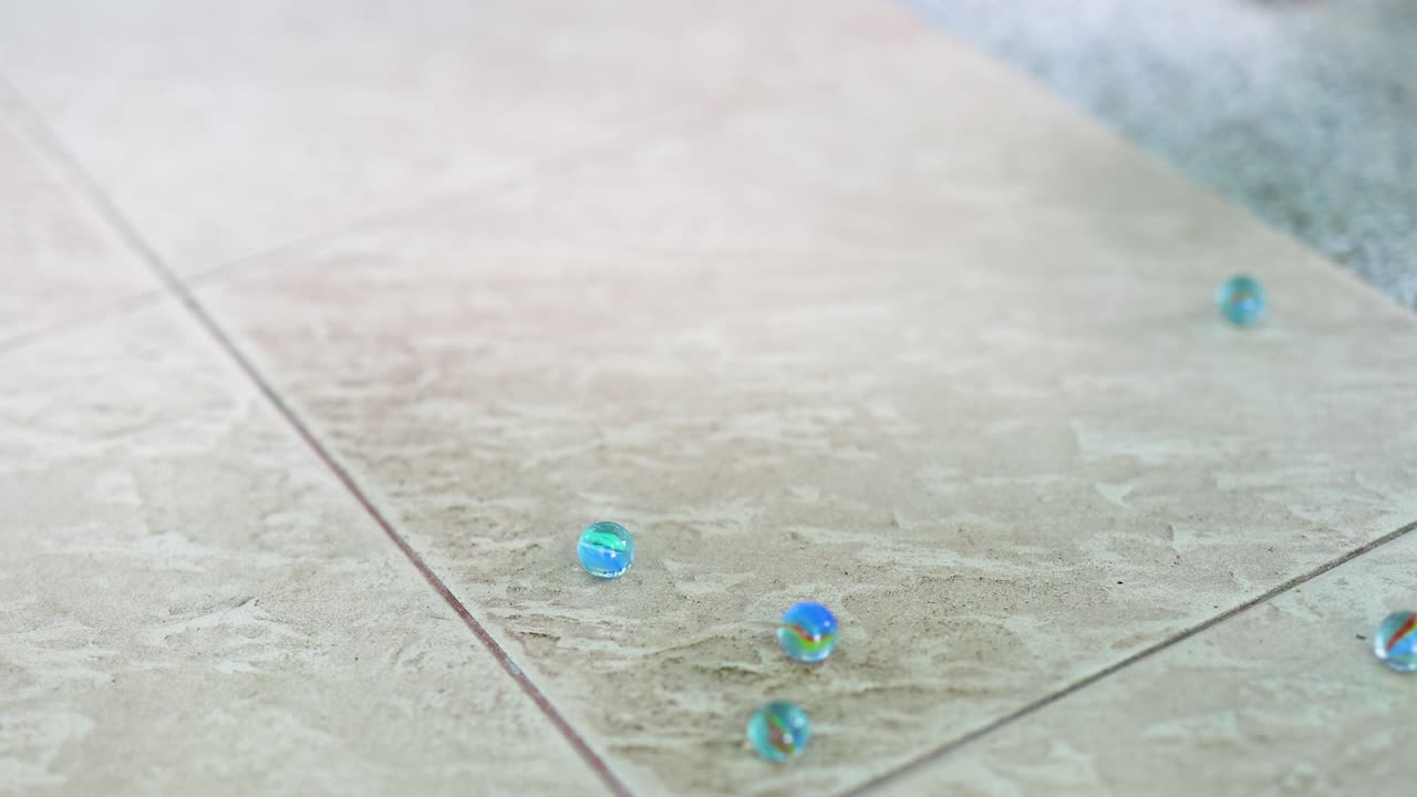 Hands gently release marbles onto a tiled floor, creating a playful, dynamic scene with natural lighting in Phuket, Thailand