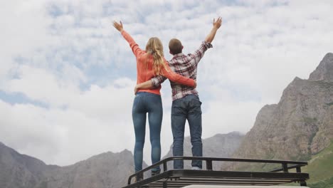 pareja caucásica pasando un buen rato en un viaje a las montañas, abrazándose y levantando las manos