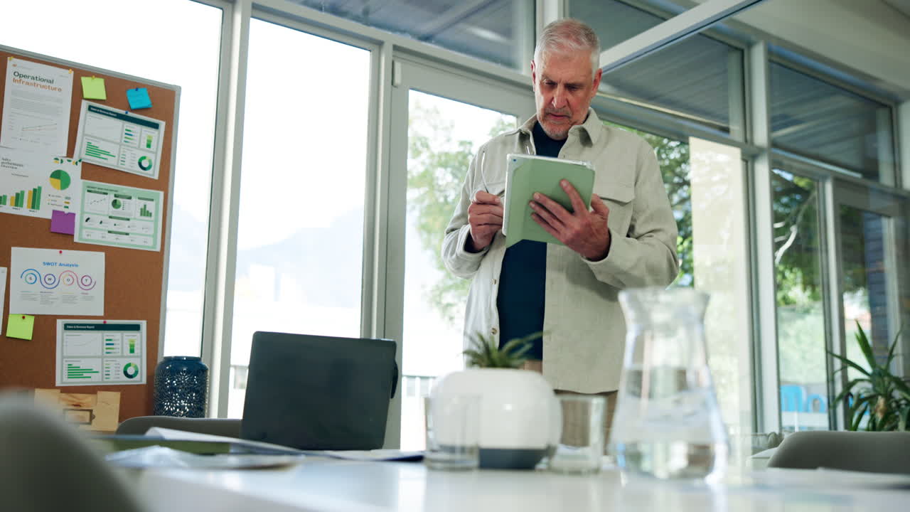 Ældre forretningsmand, der står og gennemgår data på en digital tablet.