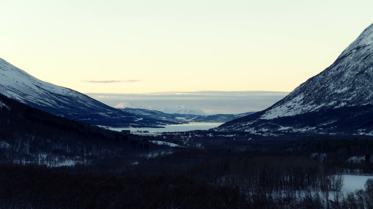 Remote snow covered valley and mountains during polar night twilight near Nordkjosbotn in northern Norway. Aerial drone panoramic view, copy space