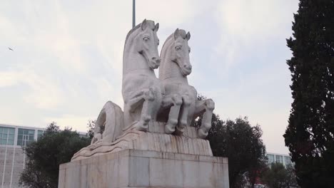 estatua de dos caballos con edificio y pájaro volando en el fondo