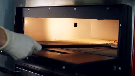Chef uses a pizza shovel to take the cooked pizza out of the oven. Opening the door of an electric oven in a restaurant kitchen