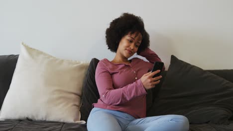 Mujer-Usando-Un-Teléfono-Inteligente-Y-Sonriendo-En-La-Sala-De-Estar