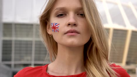 portrait of a young blonde girl soccer fan of england looking into the camera, serious face, stadium in the background 50 fps