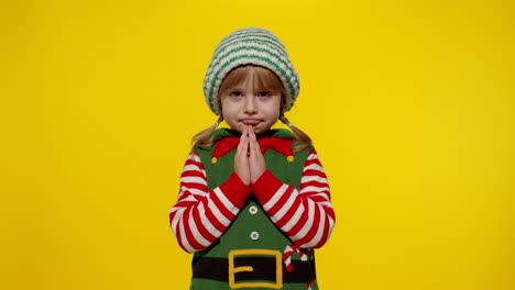 kid in christmas elf santa helper costume begs, prays about gifts on new year. keeps palms together
