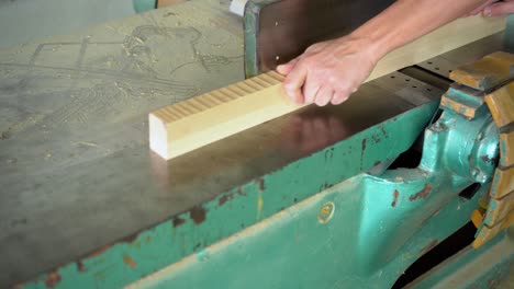 a person's hands feeding wood into a jointer machine in a workshop.