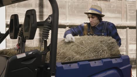 hombre trabajando cargando el heno en la caja de su vehículo todoterreno para alimentar a los animales