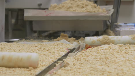 Close-up-of-multiple-workers-preparing-crumble-mix-on-top-of-confectionery-tray-bakes