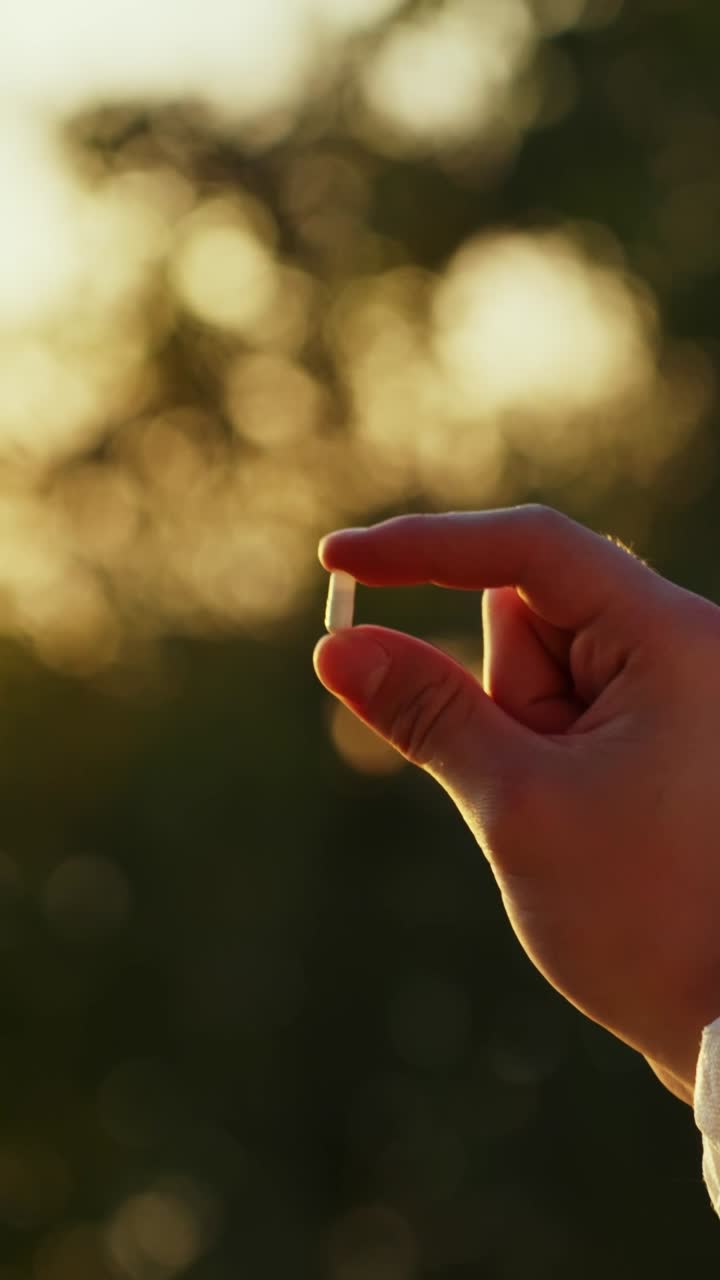 Mano che tiene un campione di pillola durante un test per la qualità ambientale con cielo luminoso sullo sfondo, tracciamento orbitale verticale