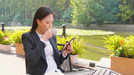 woman enjoying coffee and phone outdoors by water