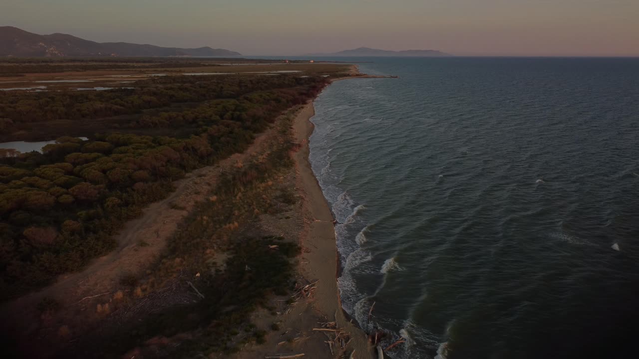 Filmato aereo epico ad alta quota con drone sopra una spiaggia sabbiosa al tramonto in riva al mare vicino a Castiglione, nell'iconico parco naturale della Maremma in Toscana, Italia, con onde, isole e un cielo rosso drammatico