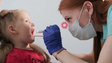 a pediatrician in a hospital examines the oral cavity and throat of a little girl.