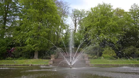 Ein-Laufender-Brunnen-In-Der-Mitte-Eines-Ruhigen-Teichs-Unter-Einem-Blauen-Bewölkten-Himmel-Während-Der-Frühen-Sprintzeit