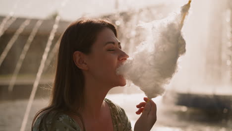 Attraktive-Frau-Isst-Zuckerwatte-Vor-Verschwommenem-Brunnen