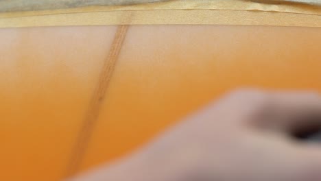 close-up of orange spray paint on wood with masking tape