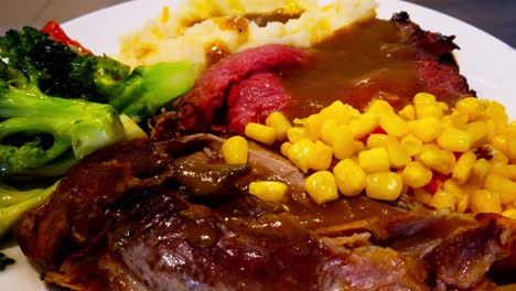 Thanksgiving-Christmas-plate-closeup-rotating-turkey-leg-roast-beef-with-gravy-steamed-broccoli-mashed-potato-and-peaches-n-cream-corn-on-a-white-ceramic-dish-on-a-wooden-table